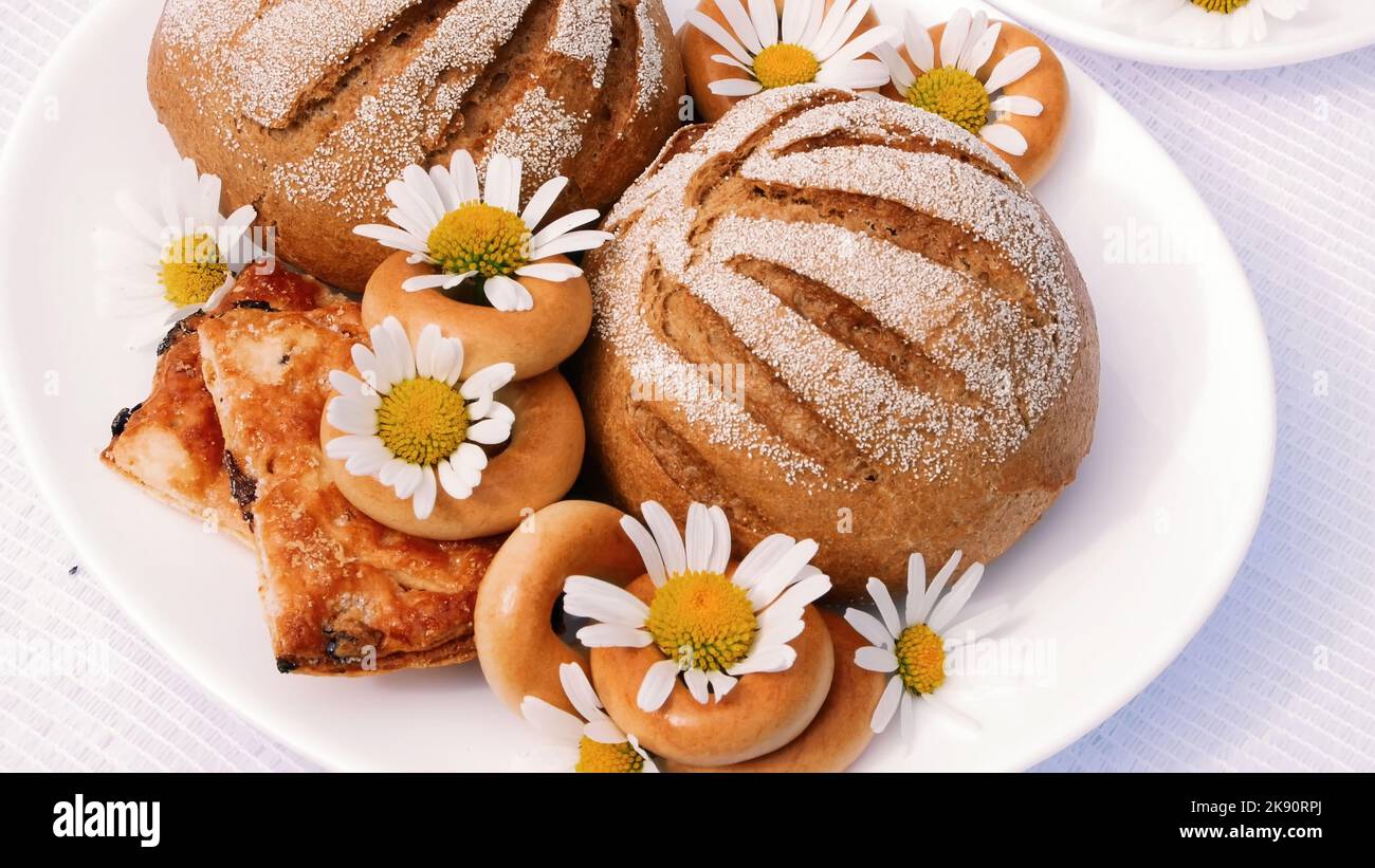Un gros plan, une assiette blanche avec des pâtisseries, des biscuits et des biscuits, décorée de pâquerettes blanches. Sur les soucoupes blanches, il y a deux tasses blanches avec du thé de camomille. Photo de haute qualité Banque D'Images