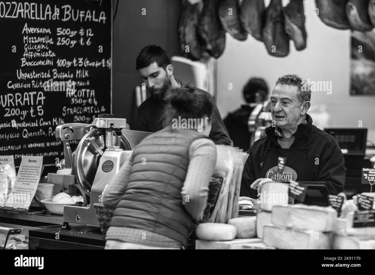 Le vendeur de fromage servant le client au Borough Market, Londres, Royaume-Uni, échelle de gris Banque D'Images