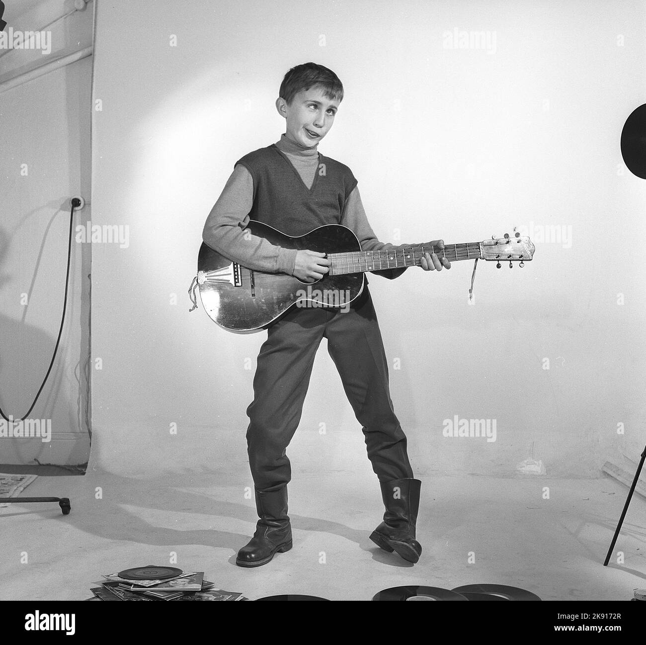 Garçon dans les 1950s. Un garçon est photographié dans un studio et fait un visage drôle en jouant de la guitare. Peut-être la façon dont il pense des artistes Rock n' roll de l'époque. Suède 1959 Kristoffersson réf. CF62 Banque D'Images