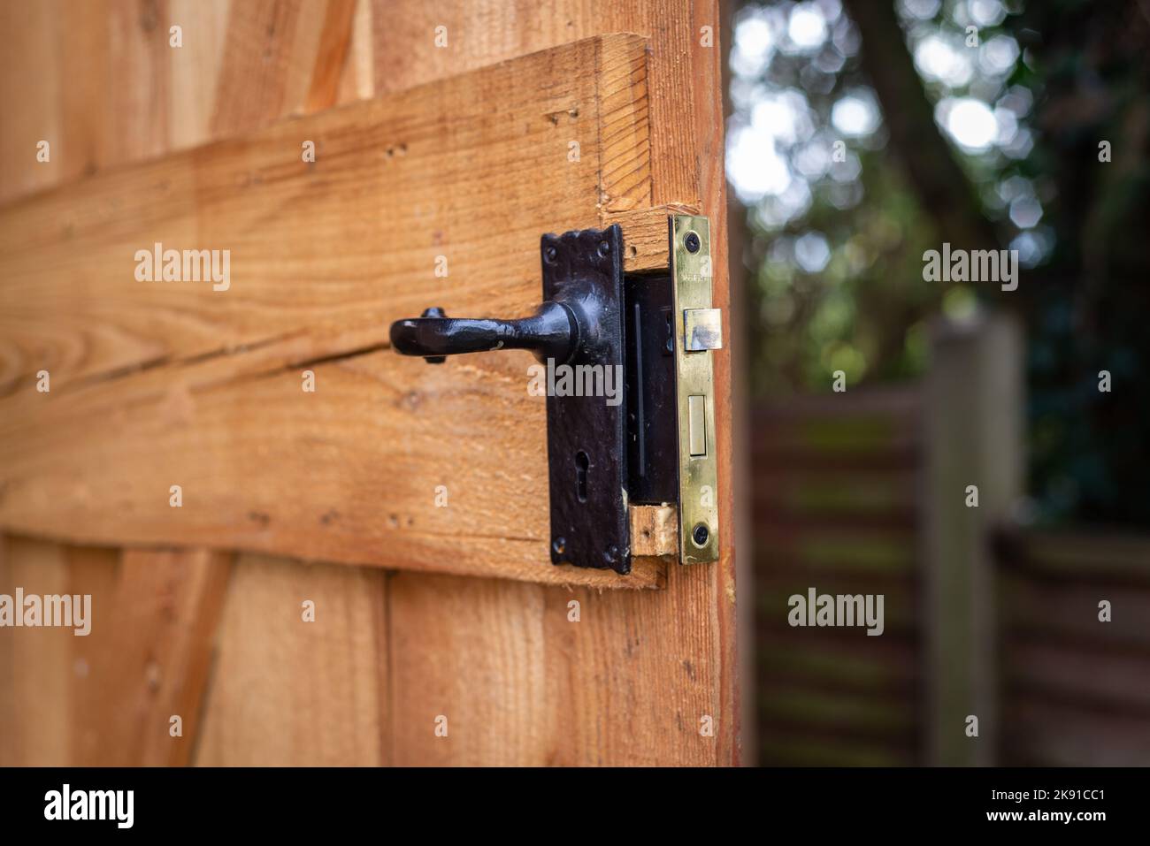 Gros plan de la poignée de porte en métal noir avec serrure encastrée sur une porte ouverte en bois dans un jardin résidentiel. Banque D'Images
