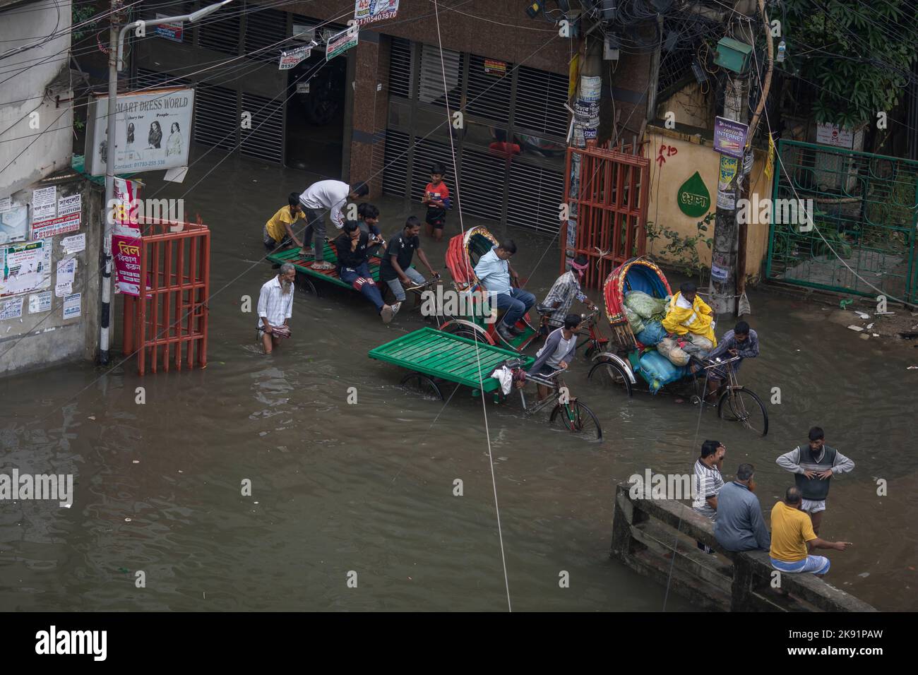 Les propriétaires de pousse-pousse ont du mal à traverser une rue engortée à la suite de fortes pluies qui causent beaucoup de souffrances aux piétons et aux navetteurs. Le cyclone Sitrang frappe le Bangladesh en train d'établir des liaisons de communication et d'alimentation, inondant les rues pour faire encore des activités. Banque D'Images