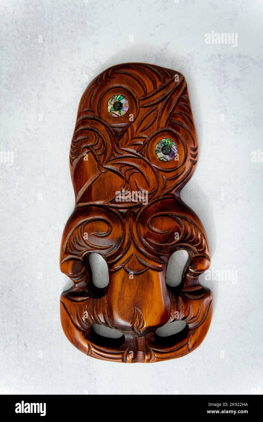 Hei Tiki en bois maori sculpté à la main avec des yeux de coquillages de paua. Taonga de Nouvelle-Zélande. Arrière-plan blanc. Banque D'Images