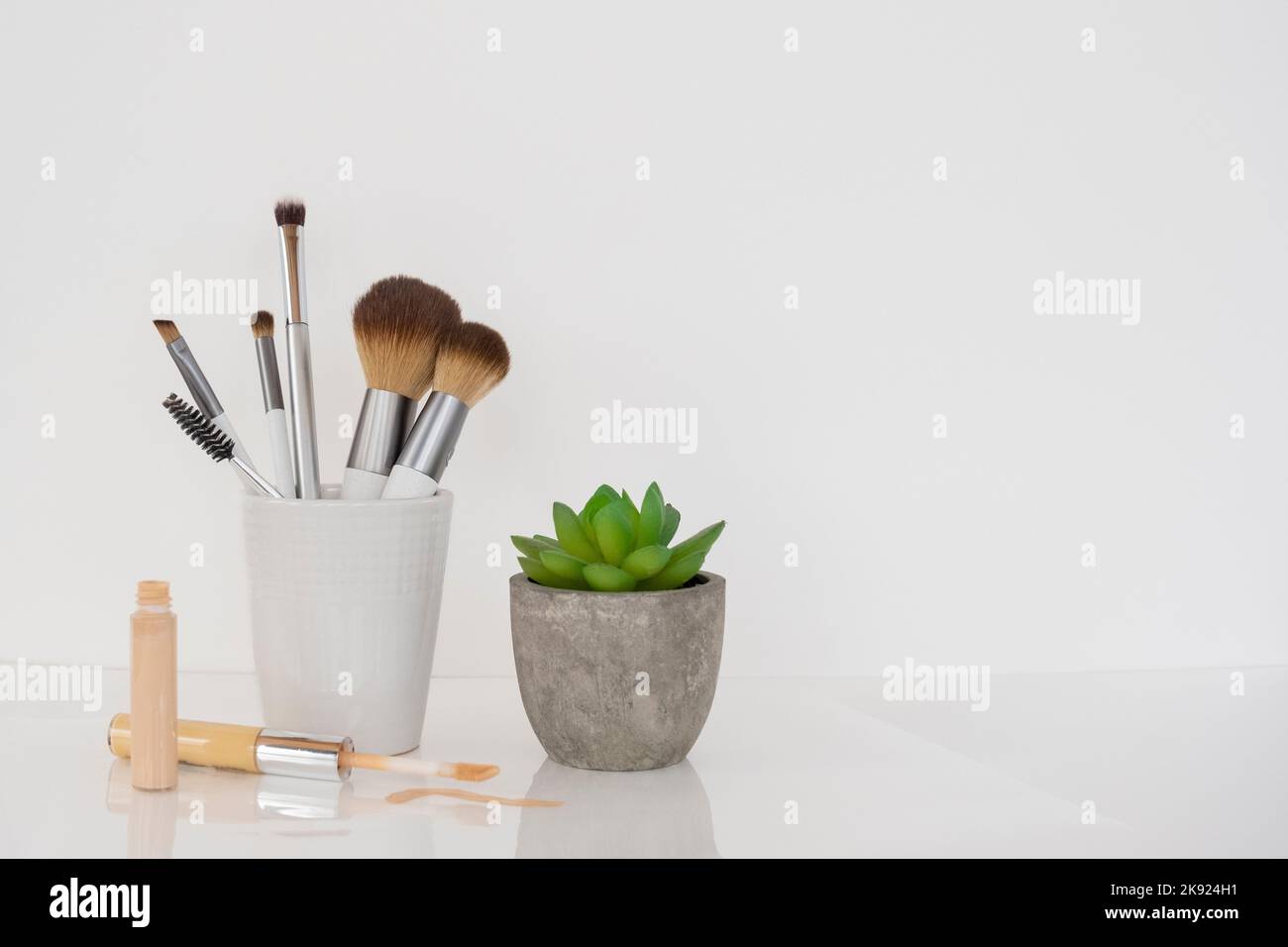 Comptoir avec pot blanc de pinceaux de maquillage, caterer, et une plante de cactus. Banque D'Images