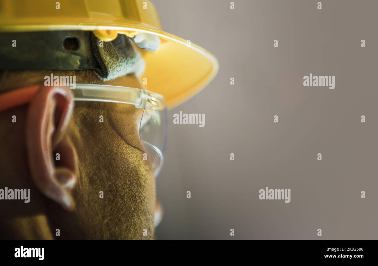 Gros plan d'un travailleur de race blanche portant un casque de sécurité jaune et des lunettes de protection. Arrière-plan solide avec espace de copie. Thème équipement de sécurité de construction. Banque D'Images