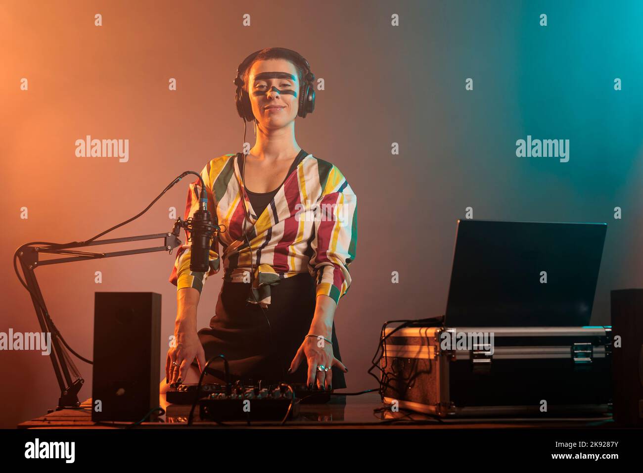 Bonne femme qui travaille comme dj avec des platines, mélangeant de la musique techno avec des basses et des équipements audio. DJ femme jouant des chansons au mélangeur, debout sur fond coloré avec de la fumée. Banque D'Images