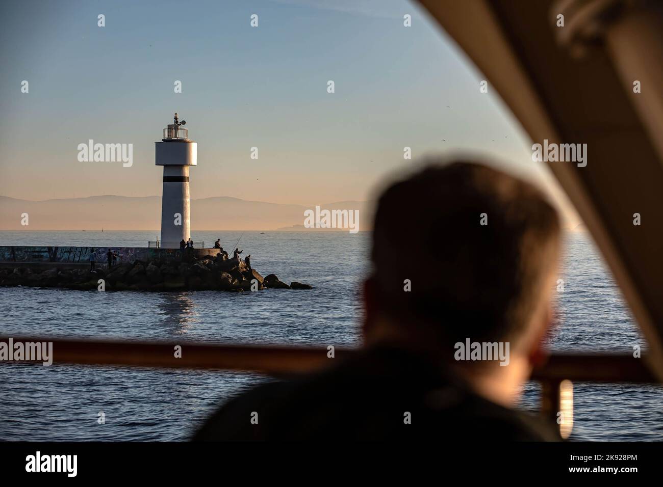 Un passager observe les lignes de ferry de la ville qui s'approchent de la jetée de Kadikoy avec le phare d'Inciburu en arrière-plan au coucher du soleil. Banque D'Images