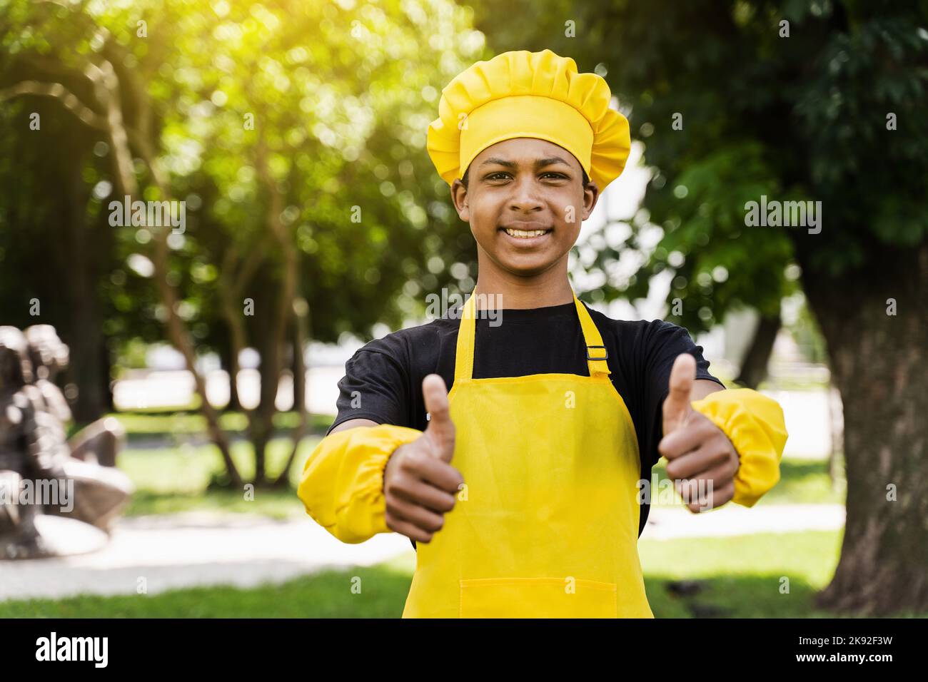 Un jeune cuisinier africain noir montrant les pouces dans le chapeau de  chef et le tablier jaune uniforme pâte de cuisson pour la boulangerie.  Publicité créative pour un café ou un restaurant