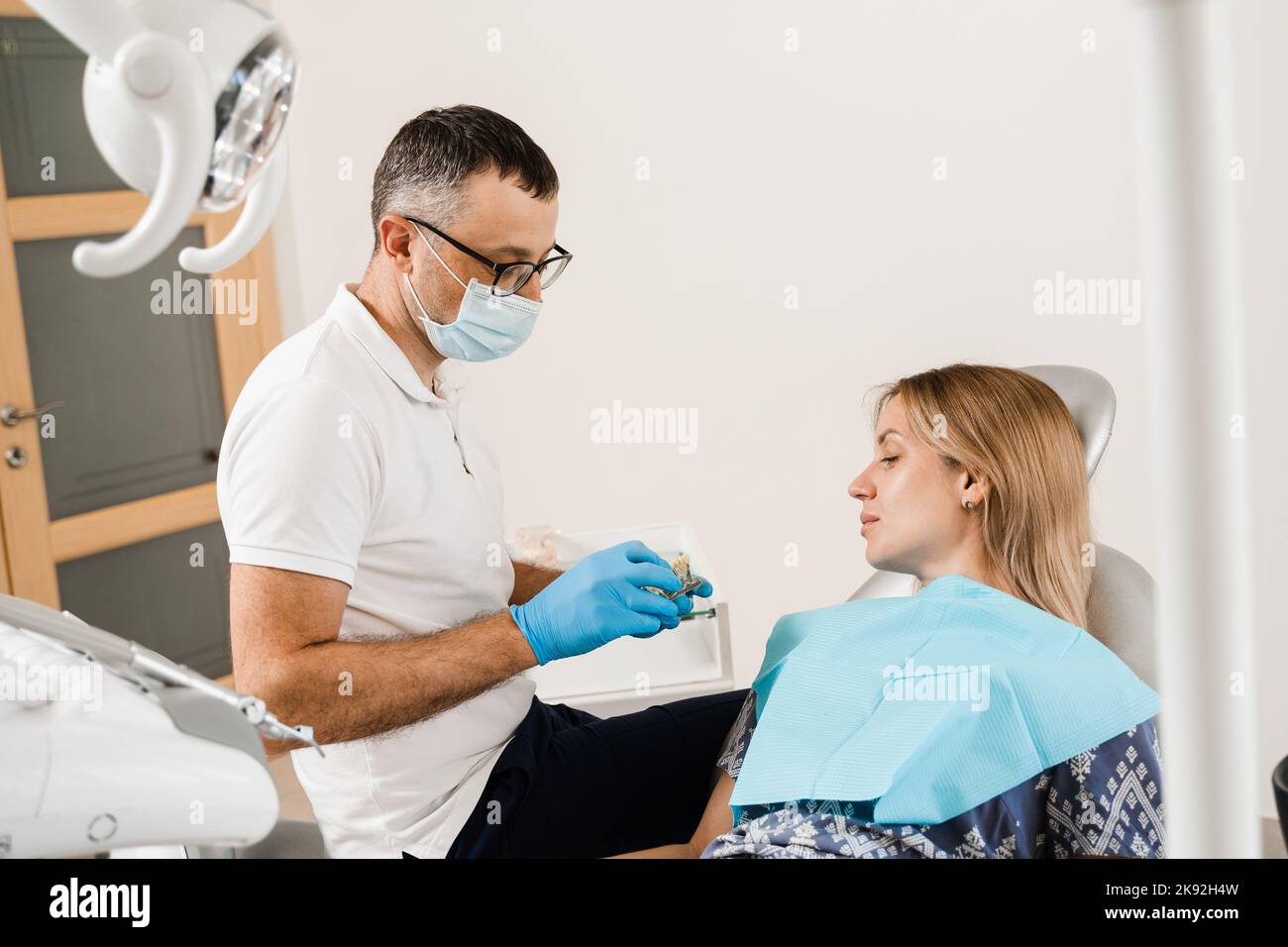 Consultation en prothèses dentaires avec un dentiste pour une patiente en dentisterie. Le médecin dentiste montre une mâchoire en plastique artificiel avec implants dentaires Banque D'Images