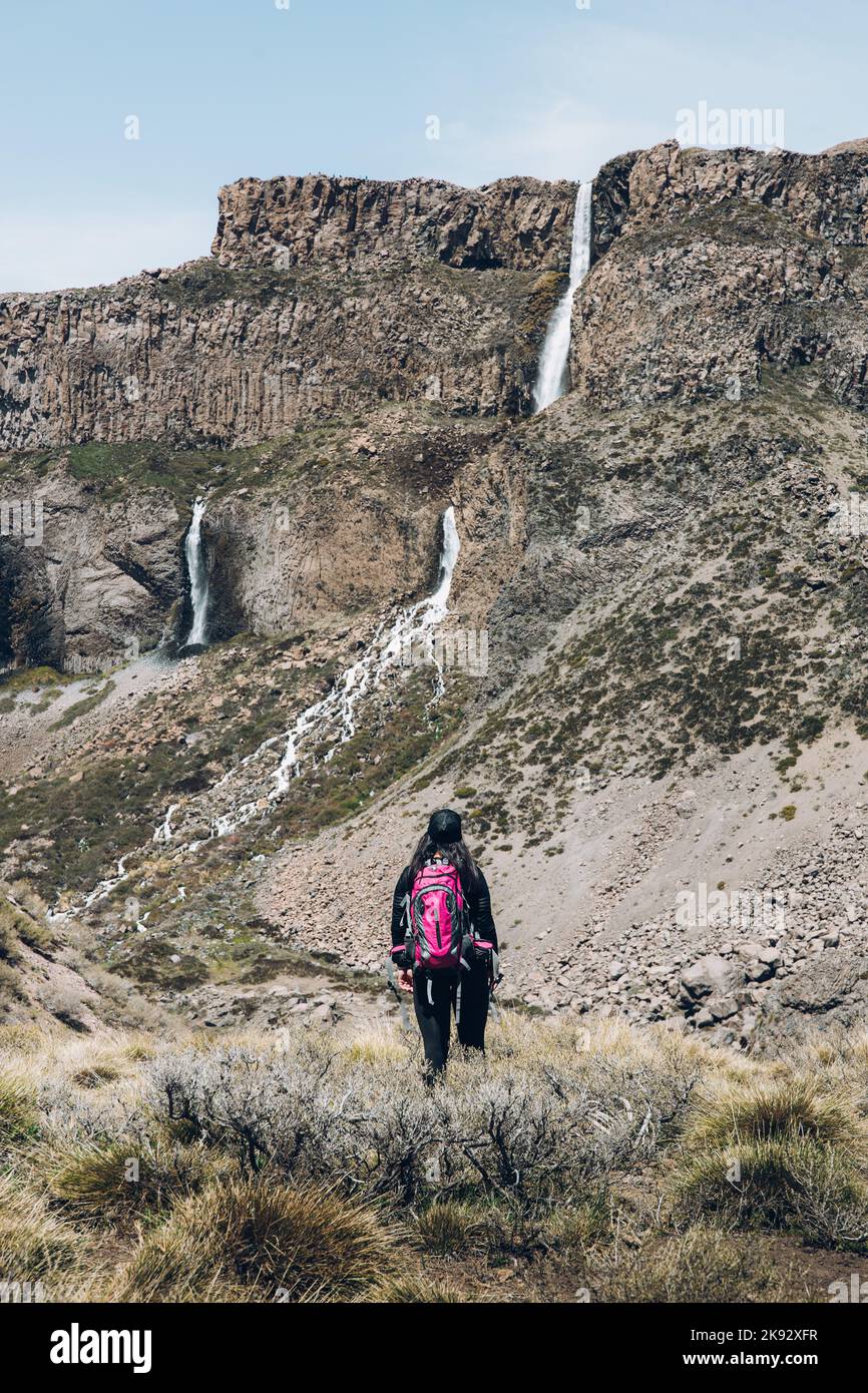 Vue arrière de la randonnée femelle Backpacker à travers un chemin rocailleux à une grande cascade. Tir vertical Banque D'Images
