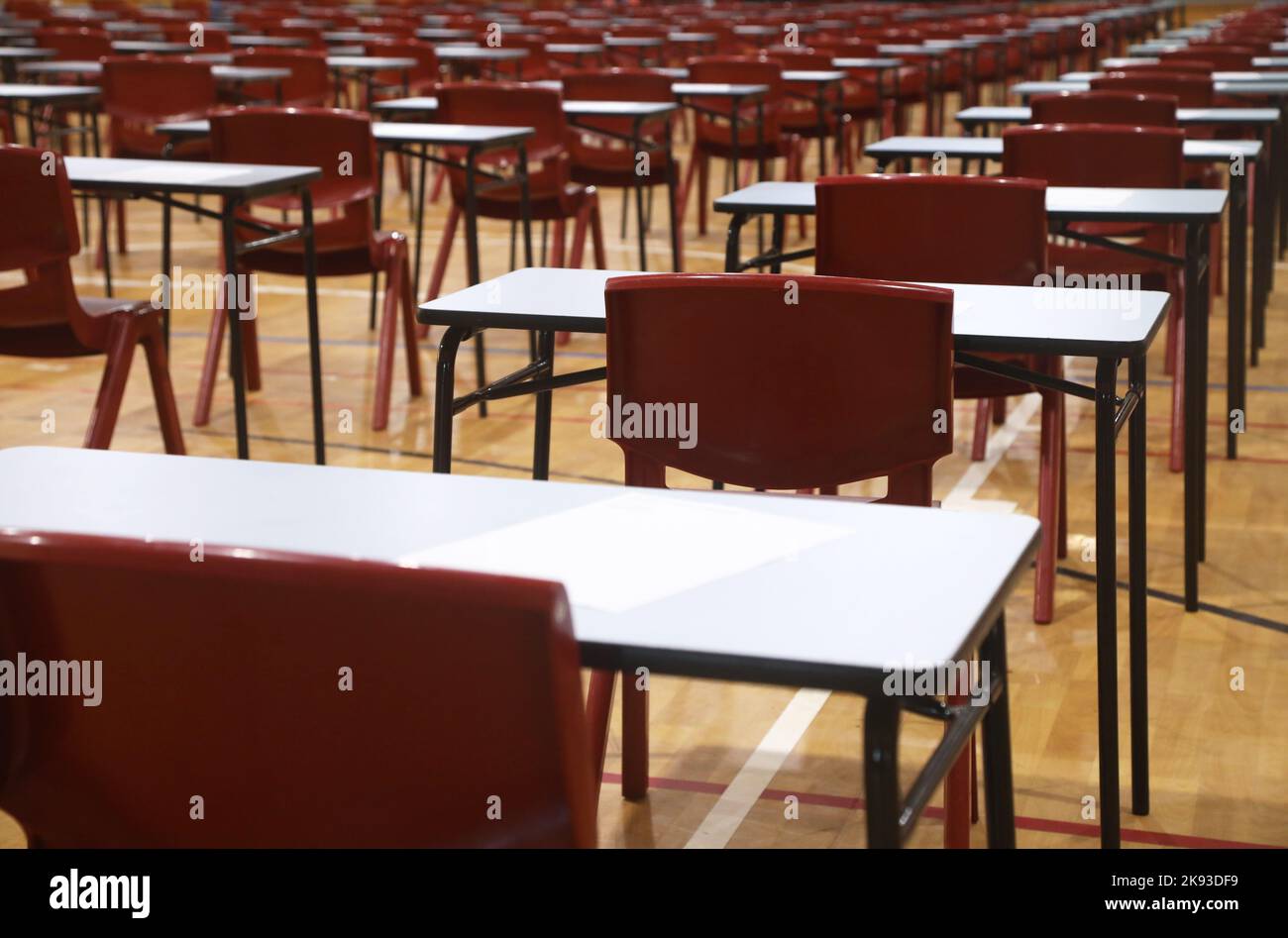 Une grande salle d'école secondaire remplie de plusieurs tables d'examen et chaises rouges organisées et prêtes pour un examen majeur ou un examen étudiant. Lignes d'ex Banque D'Images
