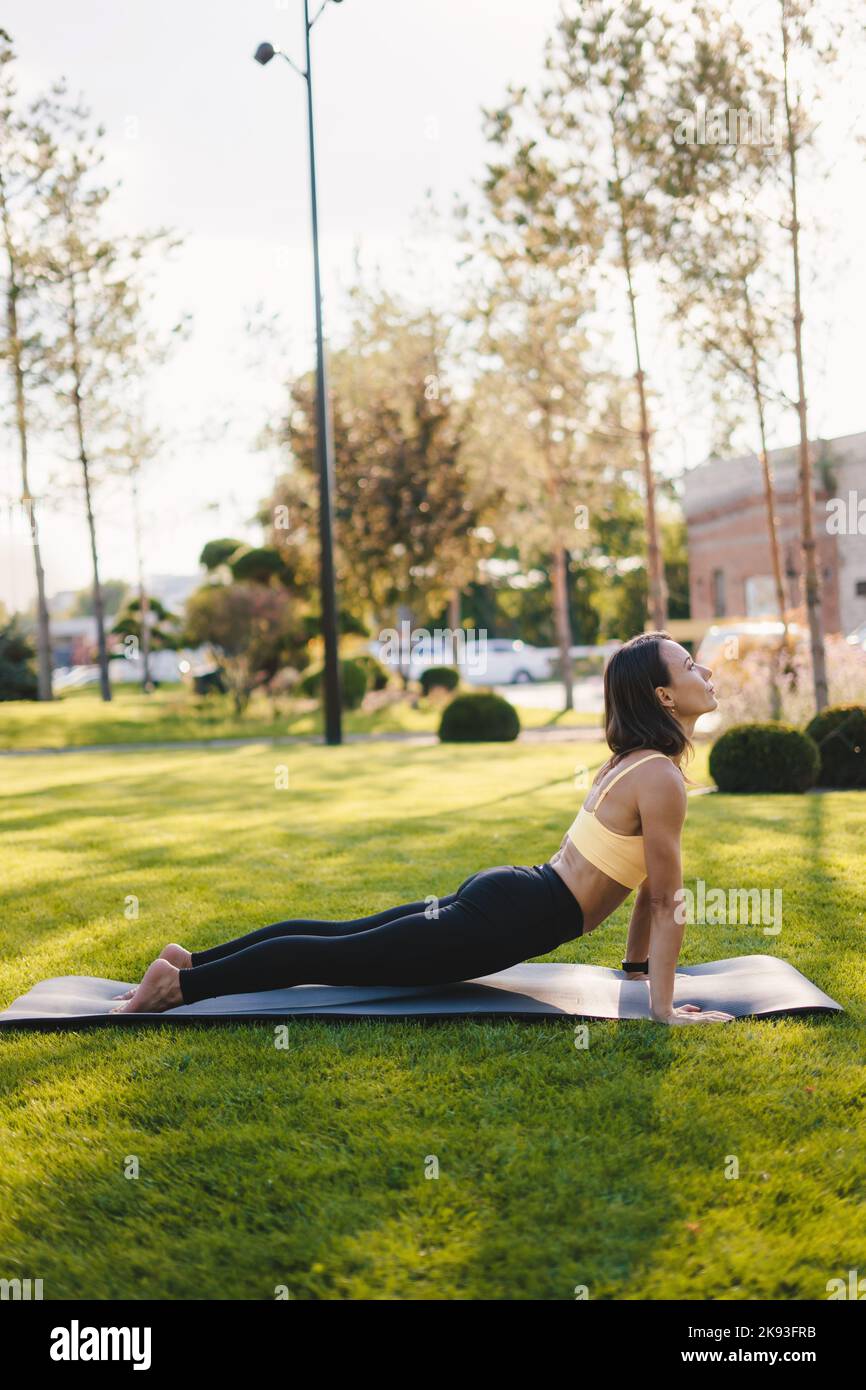 Jeune femme pratiquant l'étirement du yoga tout en faisant la posture du cobra dans le parc du matin. Un mode de vie sain et actif. Soins du corps. Entraînement. Personnes Banque D'Images