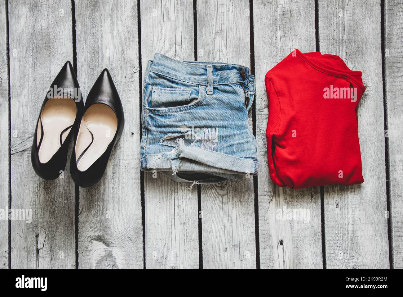 short en denim avec veste rouge et chaussures en cuir noir sur une table en bois blanc, vêtements pour femmes sur la table Banque D'Images