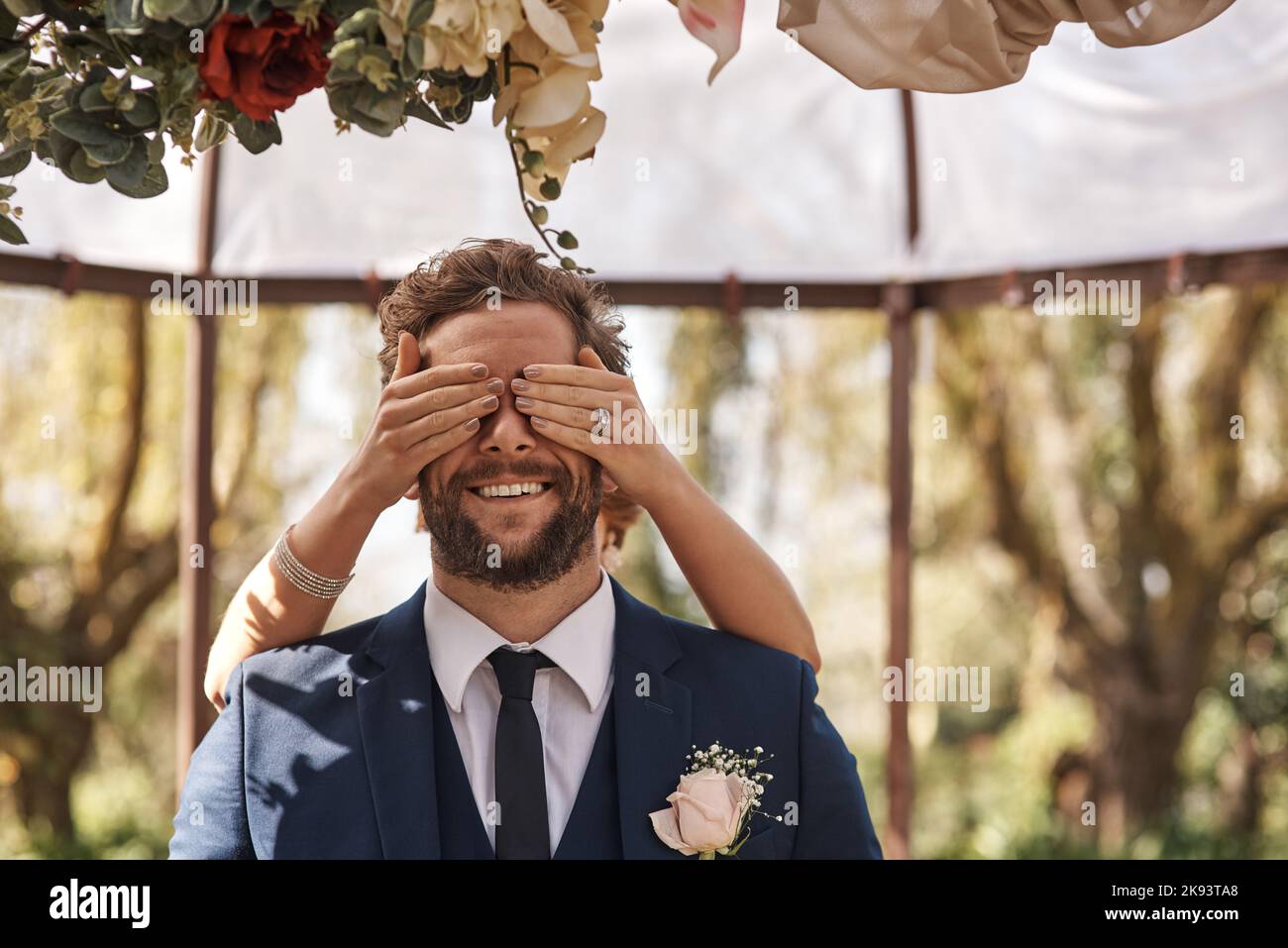 Pouvez-vous dire qui il est. Une mariée méconnaissable couvrant ses yeux de marié de derrière tout en se tenant debout à l'extérieur le jour de leur mariage. Banque D'Images