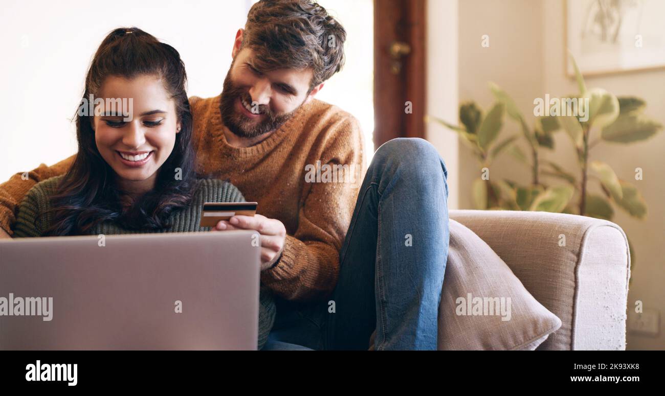 Le shopping vous fait sentir chez vous. Un jeune couple utilise un ordinateur portable et une carte de crédit sur le canapé à la maison. Banque D'Images