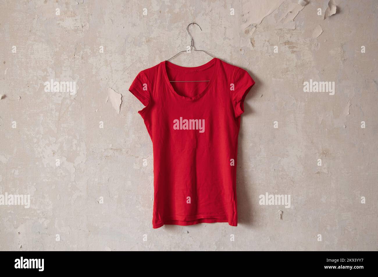 T-shirt rouge pour femmes accroché à un cintre sur un vieux mur blanc sale à la maison Banque D'Images
