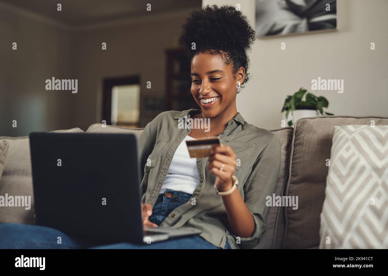 Le shopping en ligne est la façon de partir. Une belle jeune femme utilisant sa carte de crédit et son ordinateur portable tout en se relaxant sur un canapé à la maison. Banque D'Images