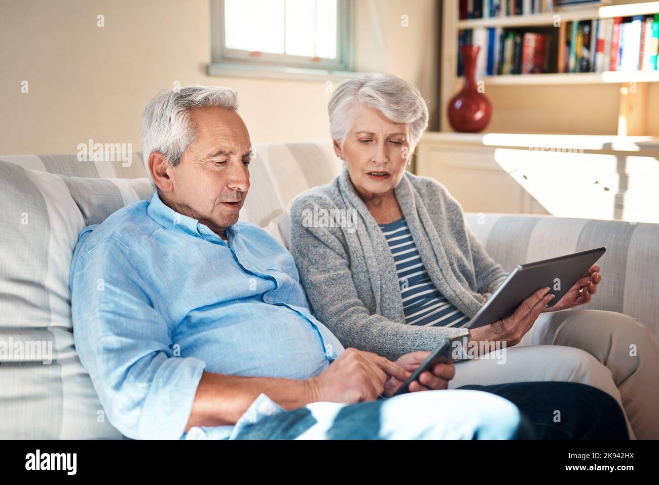 Se familiariser avec les gadgets intelligents dans leurs années d'or. Un couple senior utilisant leurs appareils intelligents sur le canapé à la maison. Banque D'Images