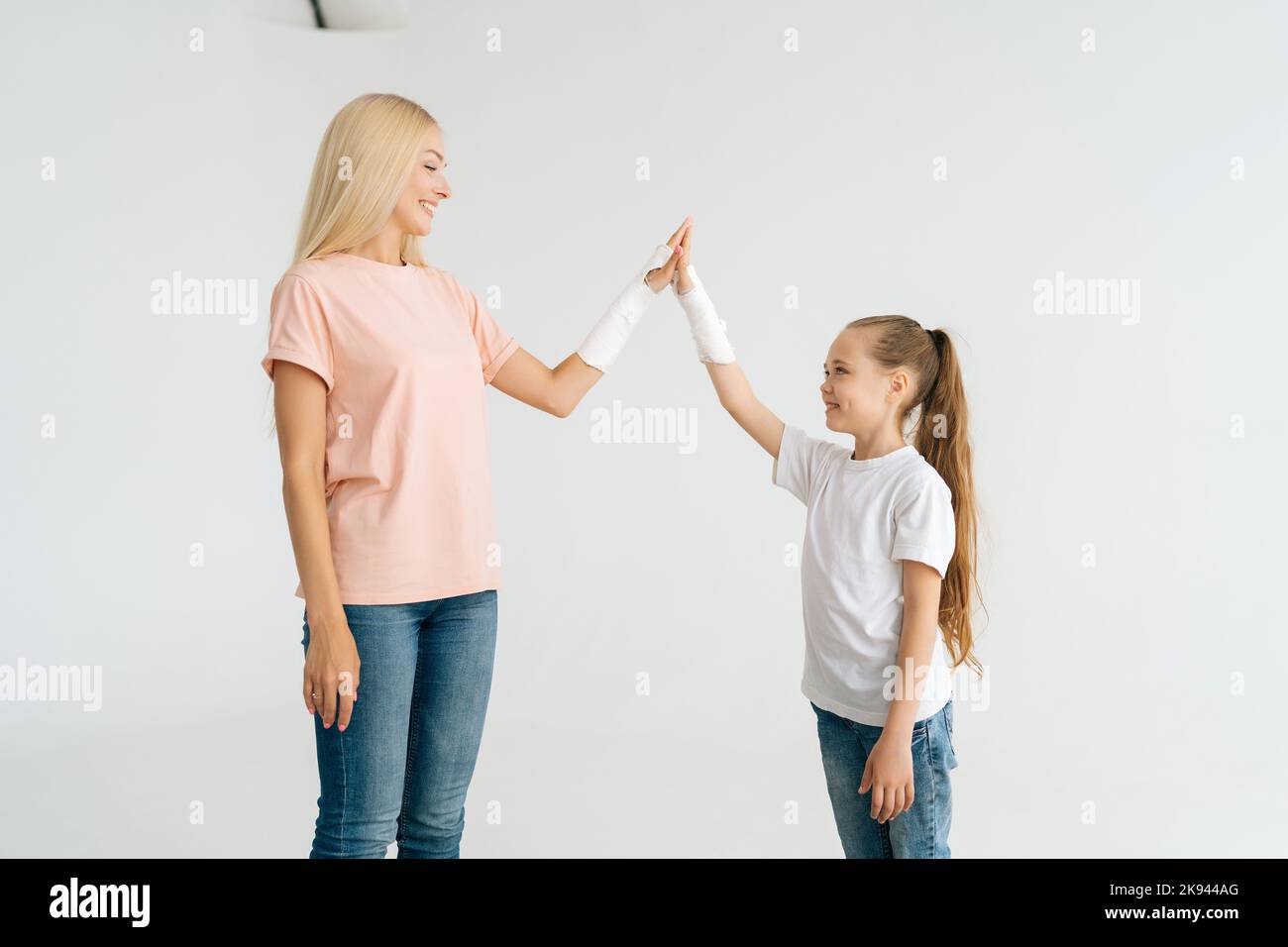 Studio portrait de drôle blessé blonde jeune femme et petite fille avec la main cassée enveloppée dans le bandage de plâtre donnant élevé cinq regardant chacun. Banque D'Images