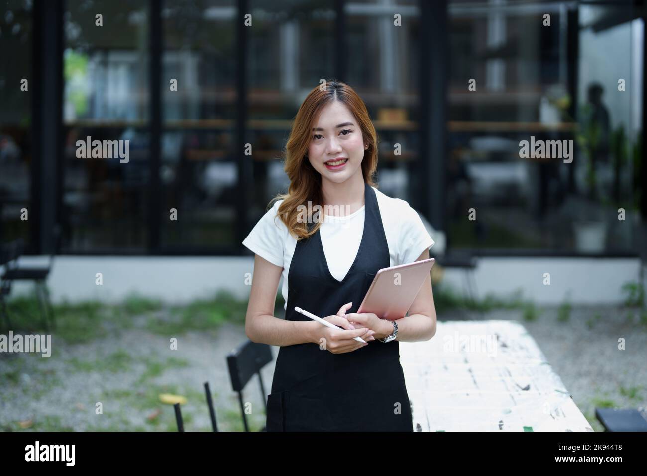 Début et ouverture d'une petite entreprise, une jeune femme asiatique montrant un visage souriant tenant une tablette dans un tablier devant un café-bar Banque D'Images