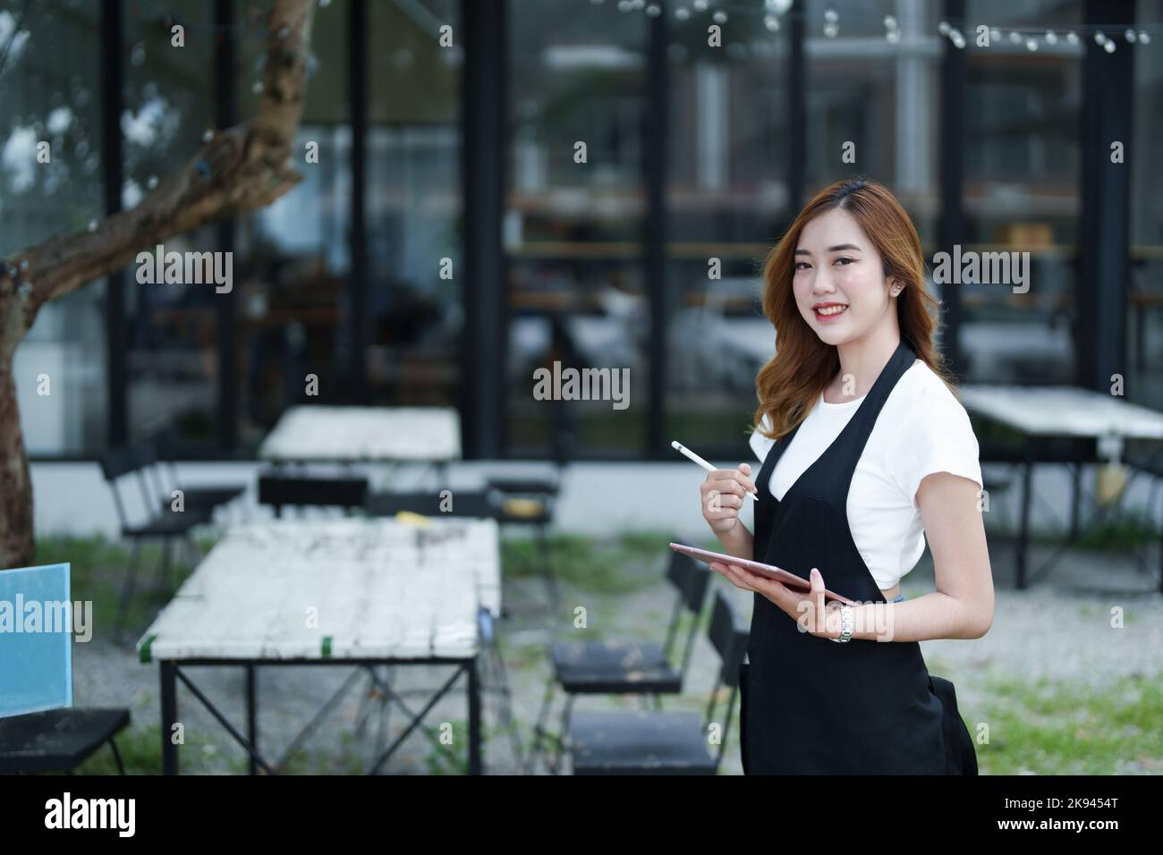 Début et ouverture d'une petite entreprise, une jeune femme asiatique montrant un visage souriant tenant une tablette dans un tablier devant un café-bar Banque D'Images