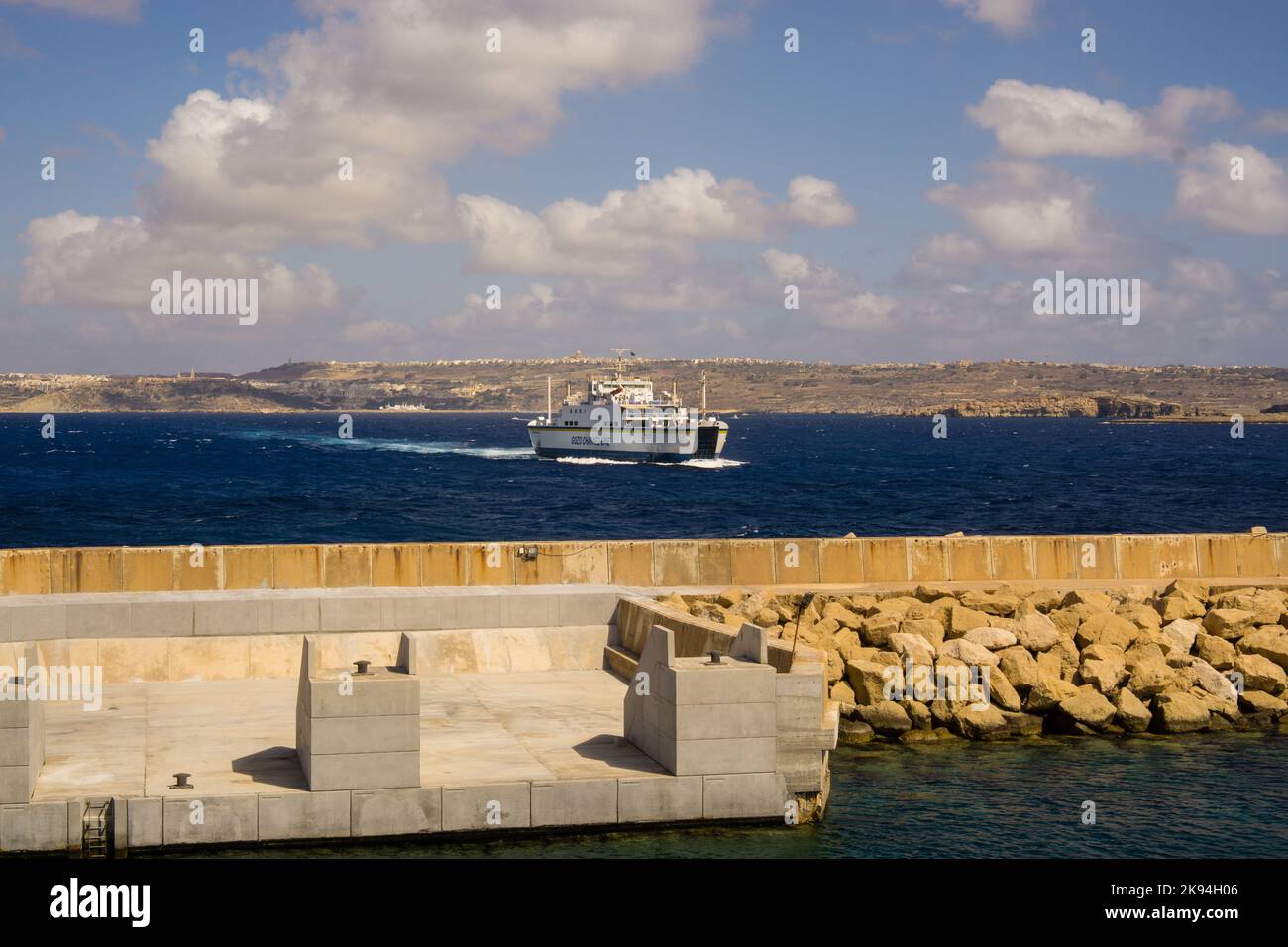 Un ferry se déplaçant à travers l'eau avec des collines et un ciel nuageux en arrière-plan. Banque D'Images