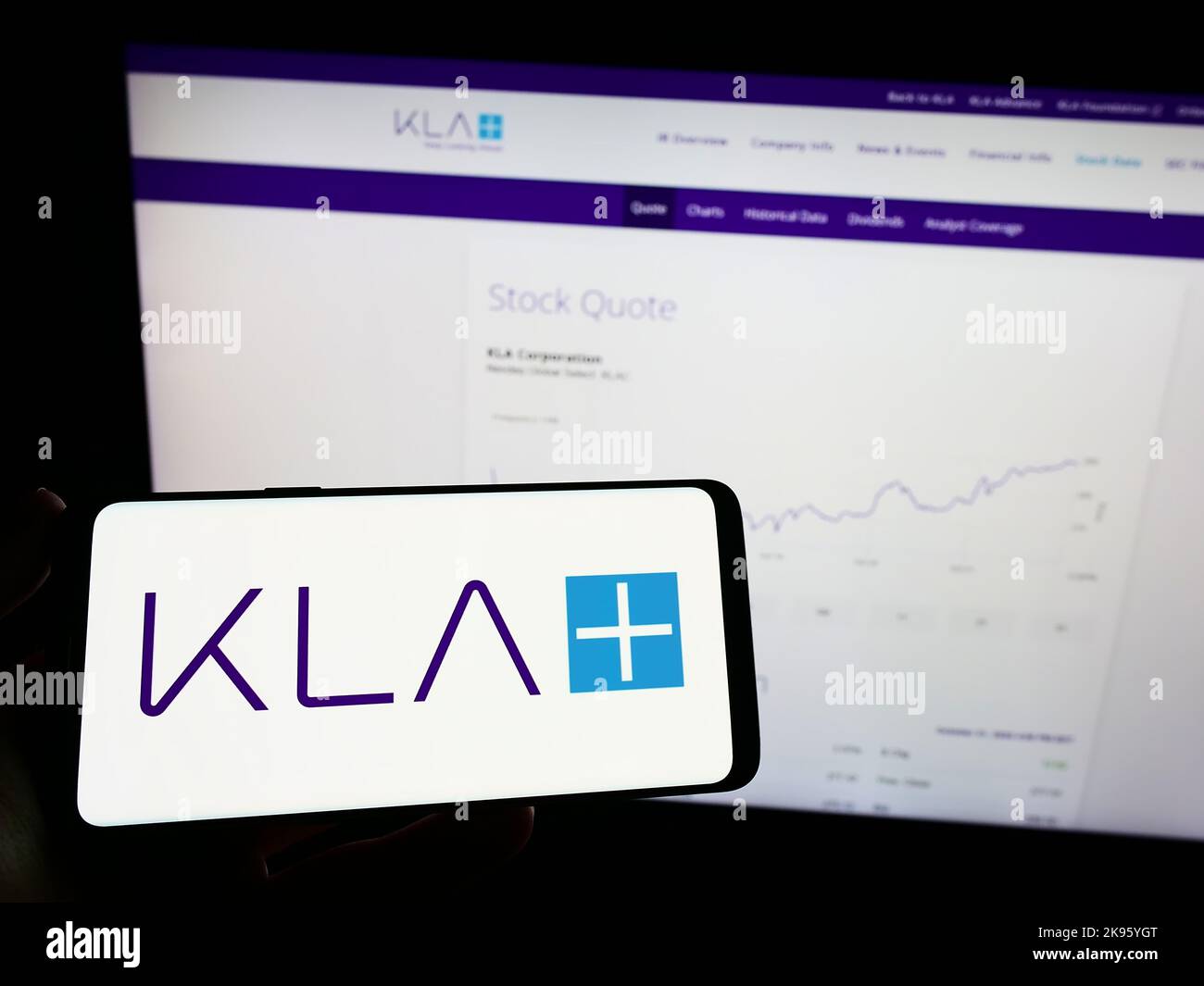 Personne tenant un téléphone portable avec le logo de la société américaine de semi-conducteurs KLA Corporation à l'écran en face de la page Web. Mise au point sur l'affichage du téléphone. Banque D'Images