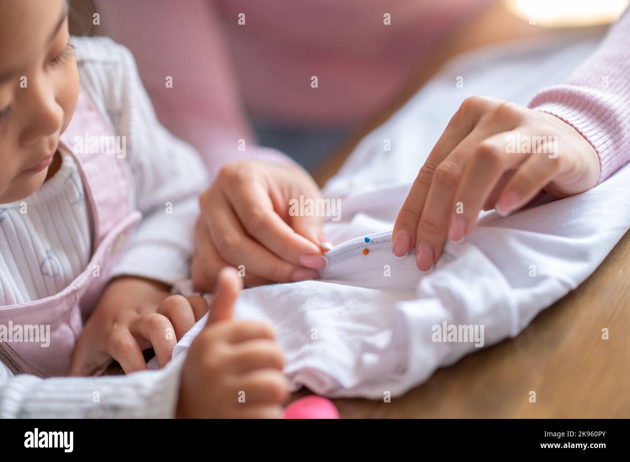 Une petite fille et sa mère piquent les coutures du tissu Banque D'Images