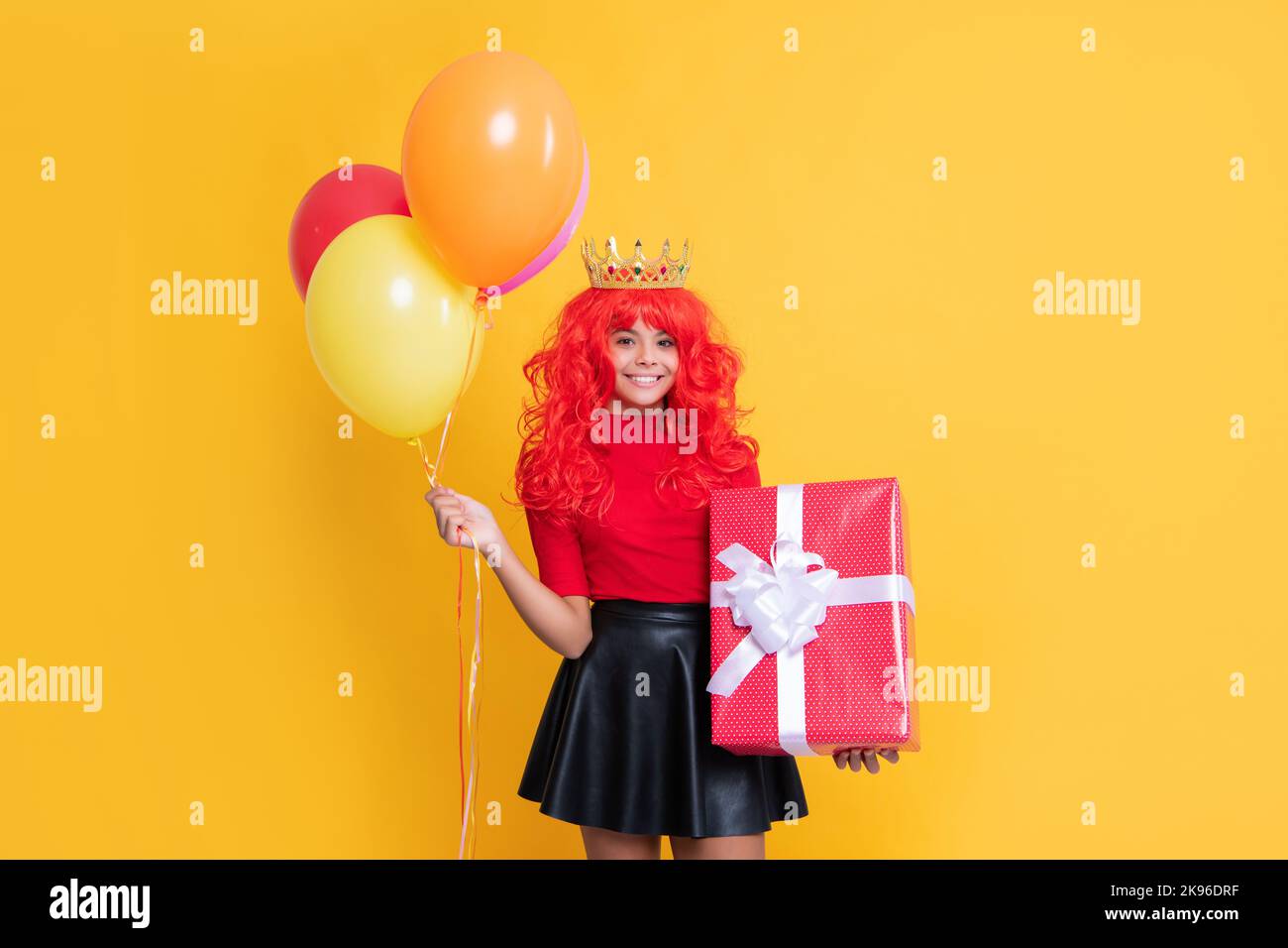 enfant gai dans la couronne avec boîte actuelle et ballon de fête sur fond jaune Banque D'Images enfant gai dans la couronne avec boîte actuelle et ballon de fête sur fond jaune Banque D'Images