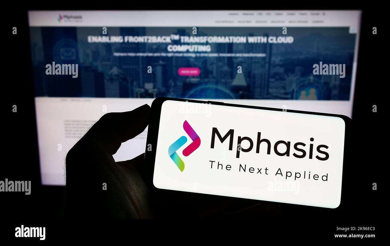 Personne tenant un téléphone portable avec le logo de la société de technologie de l'information Mphasis Limited à l'écran en face de la page Web. Mise au point sur l'affichage du téléphone. Banque D'Images