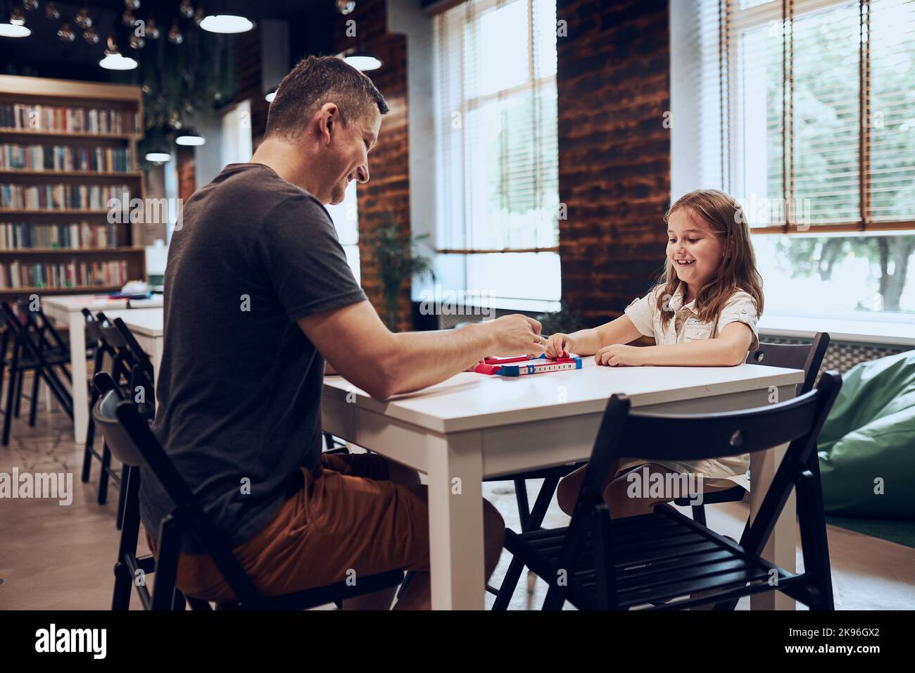 Père jouant à un jeu de société avec sa fille dans la bibliothèque publique. Enfant passant du temps avec papa après les cours à l'école primaire. Concurrence positive. FAM Banque D'Images