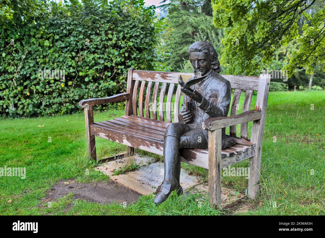 Sculpture en bronze de Gilbert White dans son jardin, assis sur un banc en bois avec un oiseau et un livre Banque D'Images