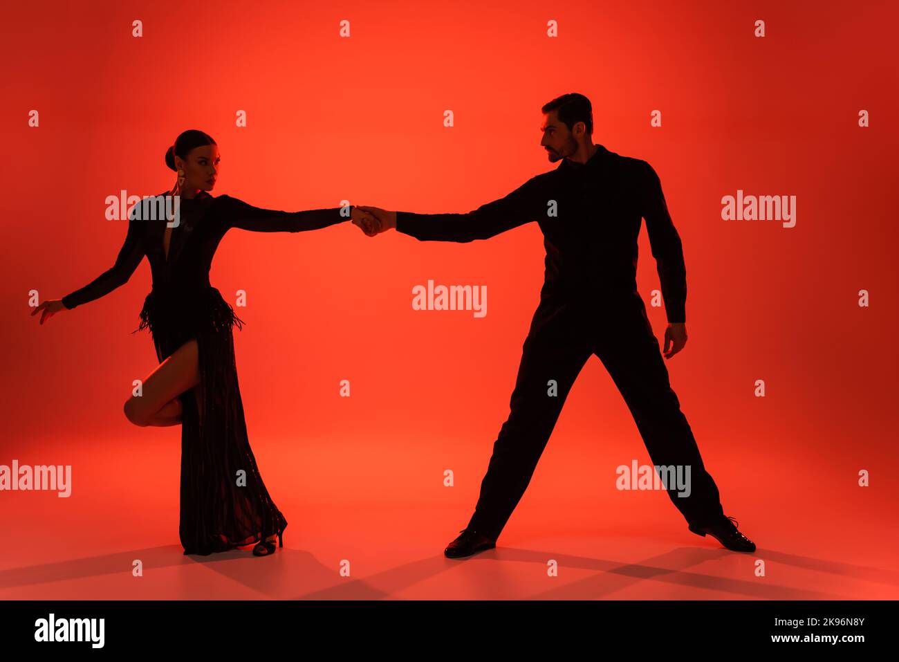 Silhouette de danseurs de salle de bal tenant les mains sur fond rouge avec ombre Banque D'Images