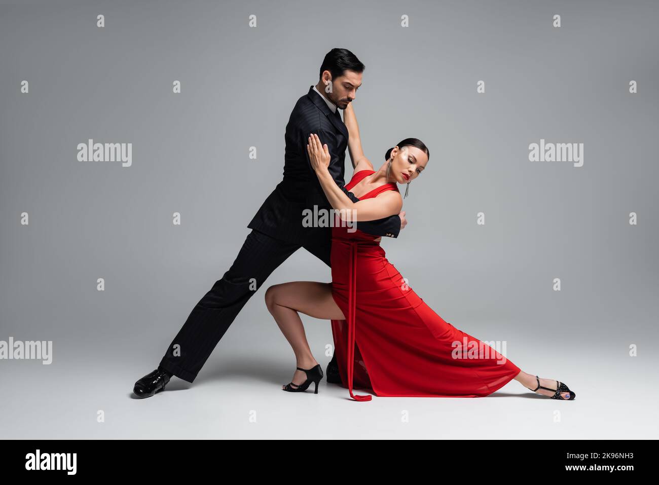Danseurs élégants en costume et en robe qui exécutent le tango sur fond gris Banque D'Images