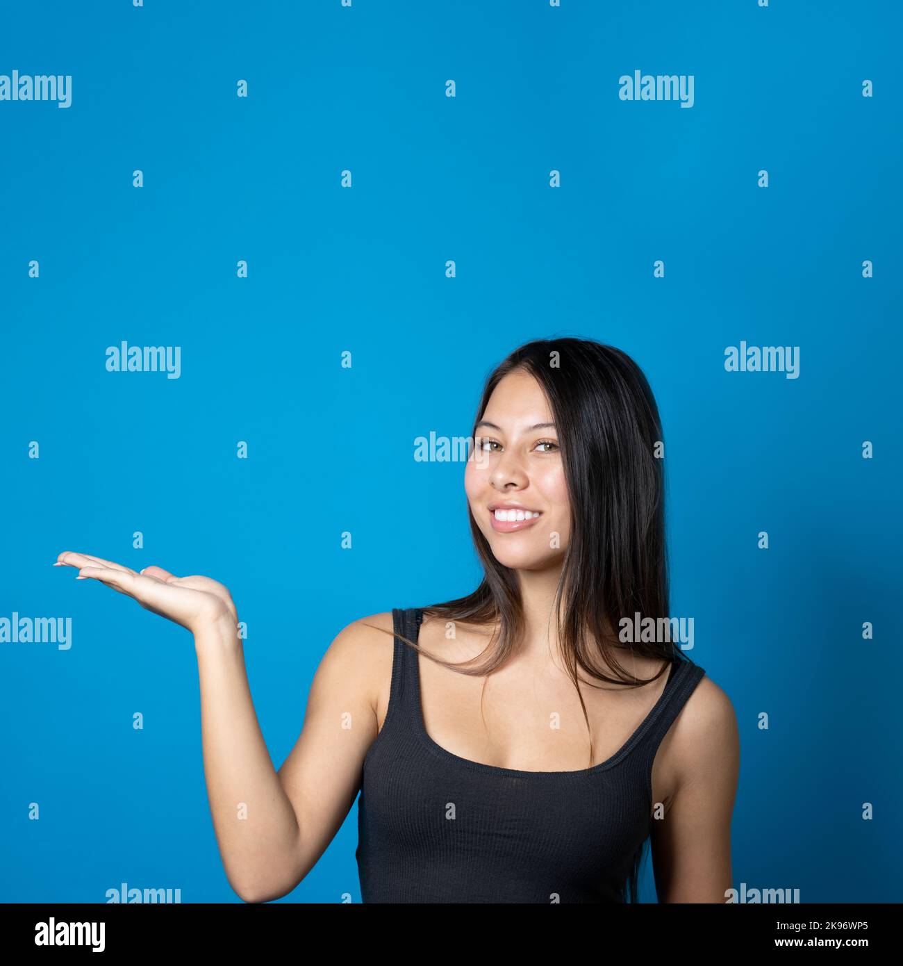 Jeune femme à la mode multiraciale avec grand sourire tenant et présentant un espace de copie sur sa paume isolée sur fond bleu Banque D'Images