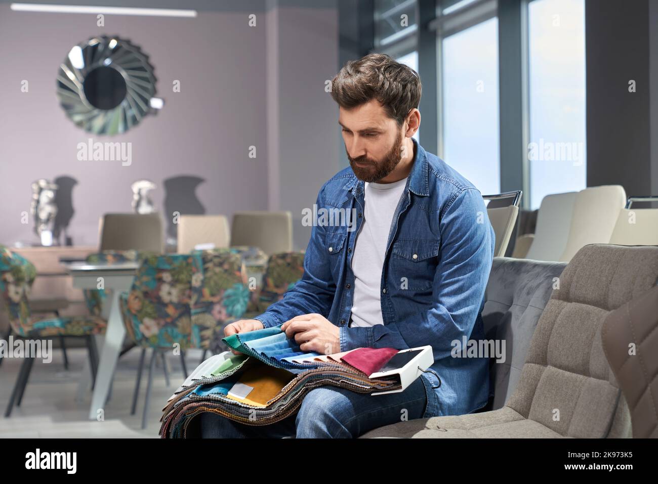Homme barbu qui choisit la couleur et la texture du tissu d'ameublement à partir de divers échantillons dans le magasin de meubles. Vue latérale d'un homme touchant le textile, faisant un choix, assis sur un canapé. Concept de conception. Banque D'Images Homme barbu qui choisit la couleur et la texture du tissu d'ameublement à partir de divers échantillons dans le magasin de meubles. Vue latérale d'un homme touchant le textile, faisant un choix, assis sur un canapé. Concept de conception. Banque D'Images