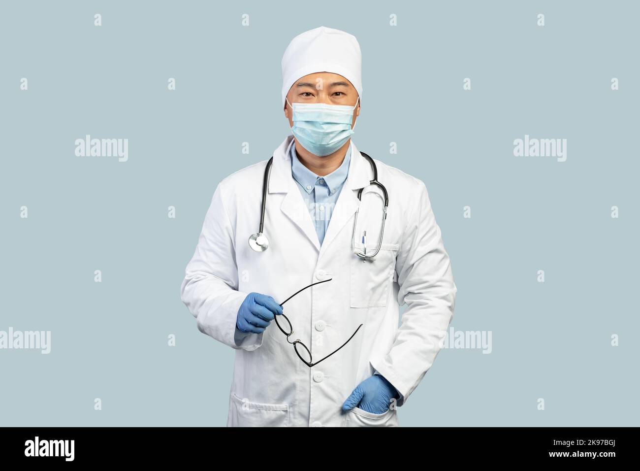 Confiant homme coréen mature médecin en manteau blanc, gants de protection, masque prend des lunettes Banque D'Images