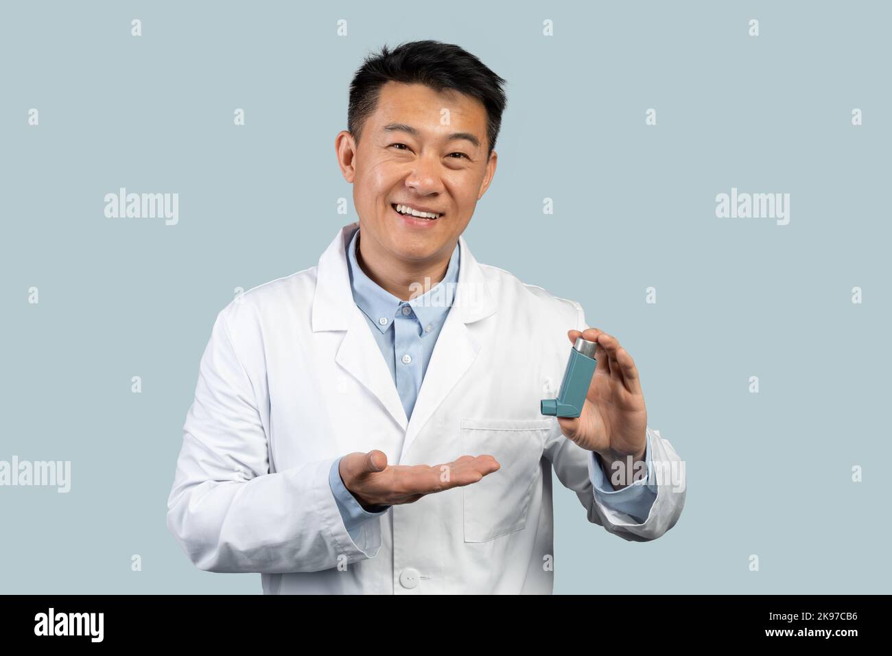 Un bon médecin asiatique d'âge moyen en manteau blanc montre un inhalateur pour les soins de santé Banque D'Images