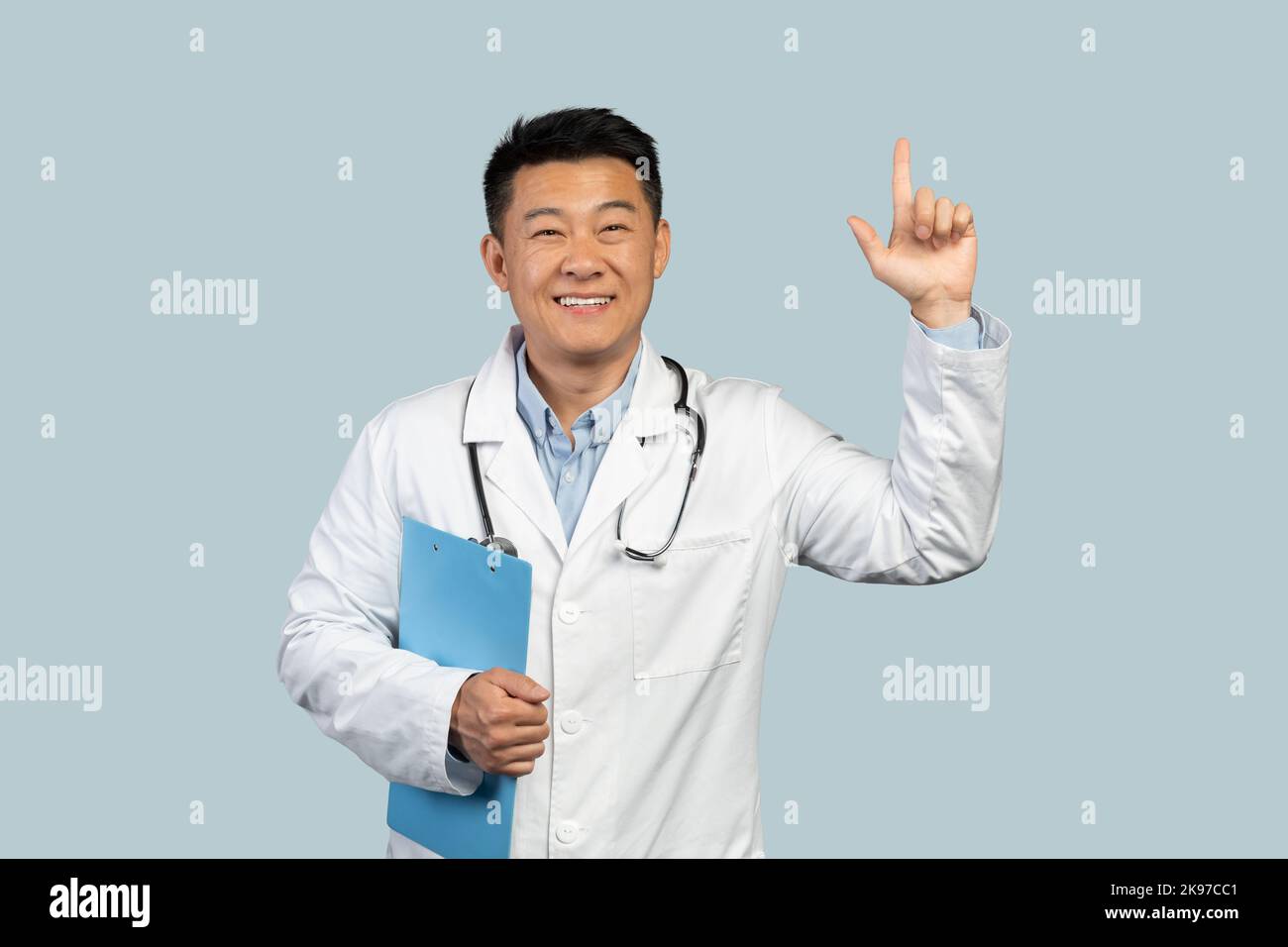 Joyeux médecin chinois d'âge moyen en manteau blanc avec stéthoscope montrant le doigt vers le haut Banque D'Images