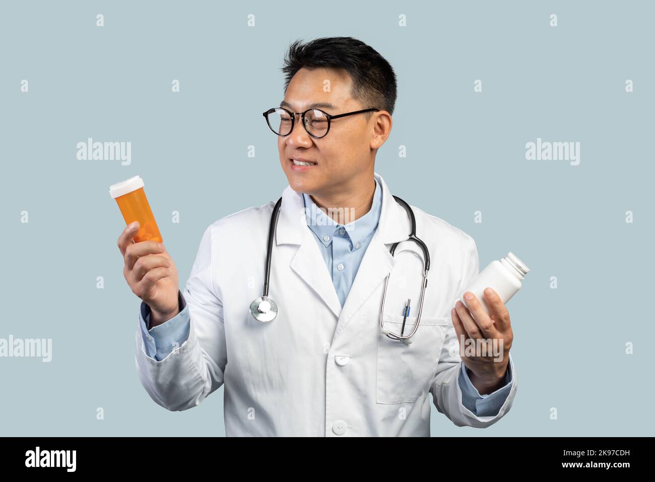 Pensive sourire mi-âge chinois médecin mâle en manteau blanc, les verres regarde des pots de pilules Banque D'Images