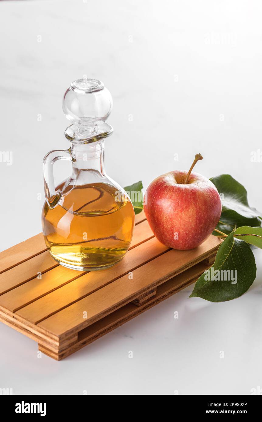 Vinaigre de cidre de pomme dans une bouteille de verre et pommes fraîches avec des feuilles sur fond clair Banque D'Images