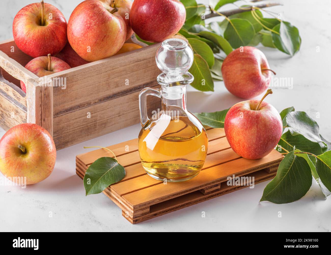 Vinaigre de cidre de pomme dans une bouteille de verre et pommes fraîches avec des feuilles sur fond clair Banque D'Images