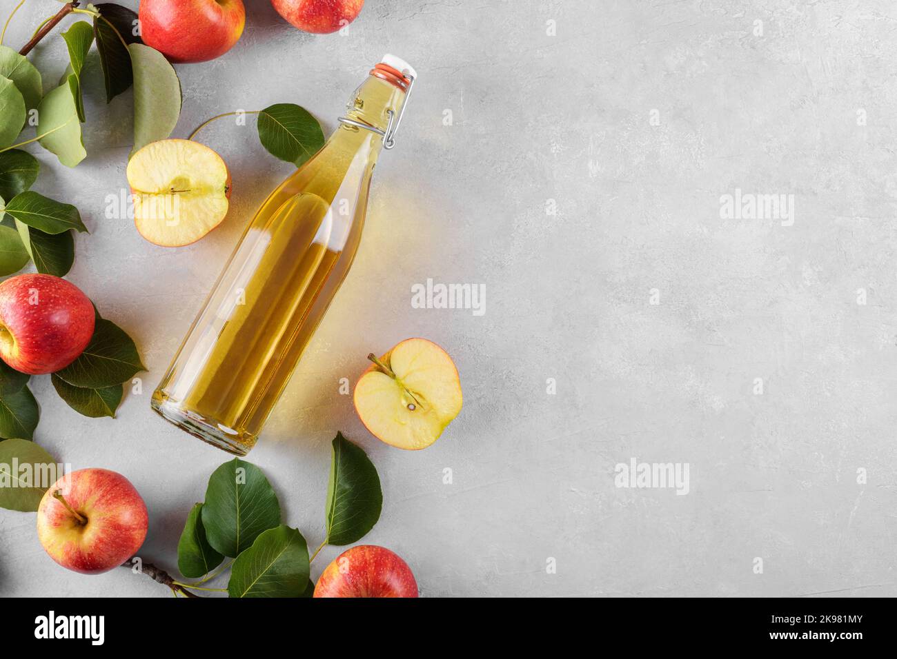 Vinaigre de cidre de pomme dans une bouteille de verre et pommes fraîches avec des feuilles sur fond clair, vue de dessus, plat Banque D'Images