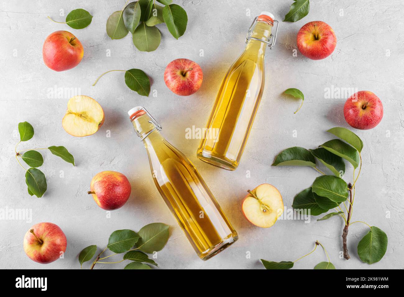 Vinaigre de cidre de pomme dans deux bouteilles de verre et pommes fraîches avec feuilles sur fond clair, vue de dessus, plat Banque D'Images