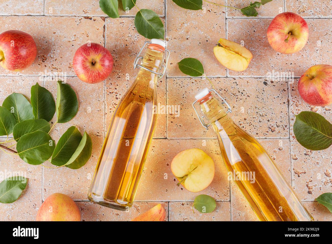 Vinaigre de cidre de pomme dans deux bouteilles de verre et pommes fraîches avec des feuilles sur fond de béton beige, vue de dessus, gros plan Banque D'Images