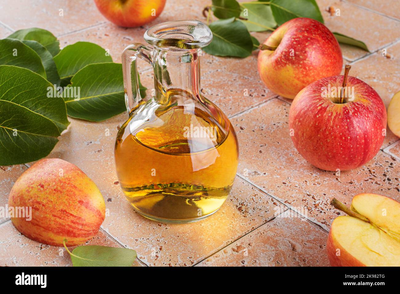 Vinaigre de cidre de pomme de fruits fermentés en bouteille de verre avec pommes sur carreaux de travertin beige fond de table Banque D'Images