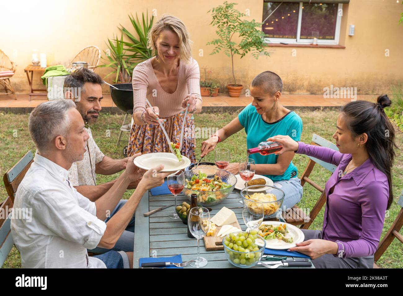 Femme sert la nourriture avec des amis riant autour de la table à l'extérieur. Banque D'Images