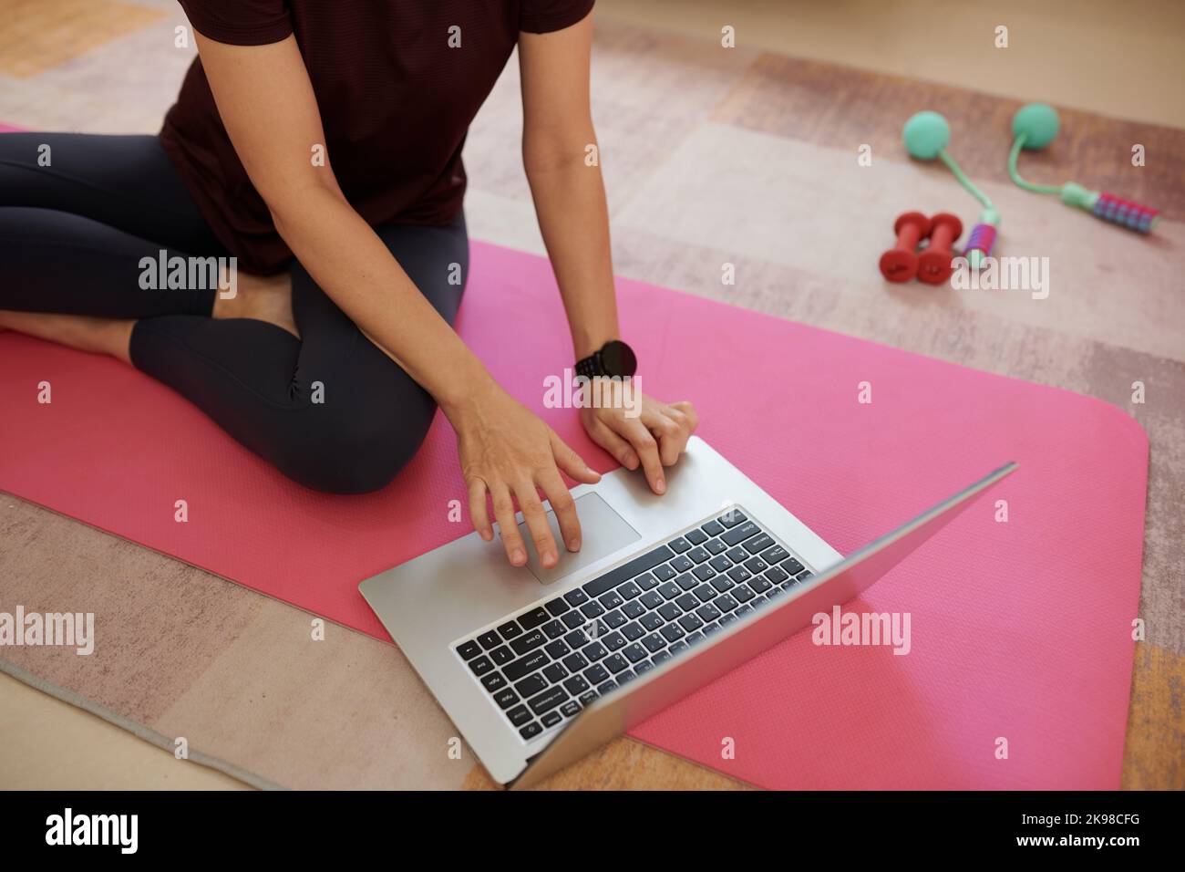 Jeune femme assise sur le tapis de yoga et à la recherche de vidéo de la forme physique préférée blogger Banque D'Images
