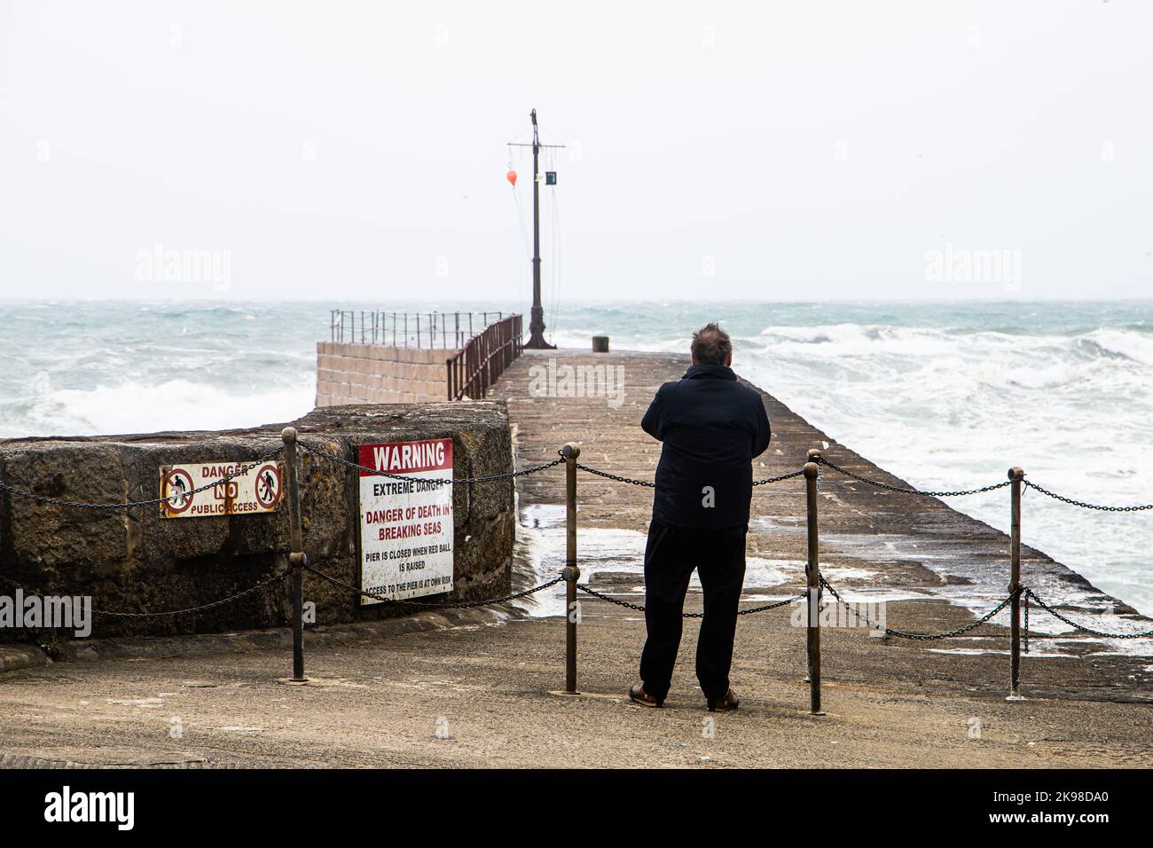 Un homme regarde la jetée du port de Porthleven, fermée en raison du mauvais temps Banque D'Images