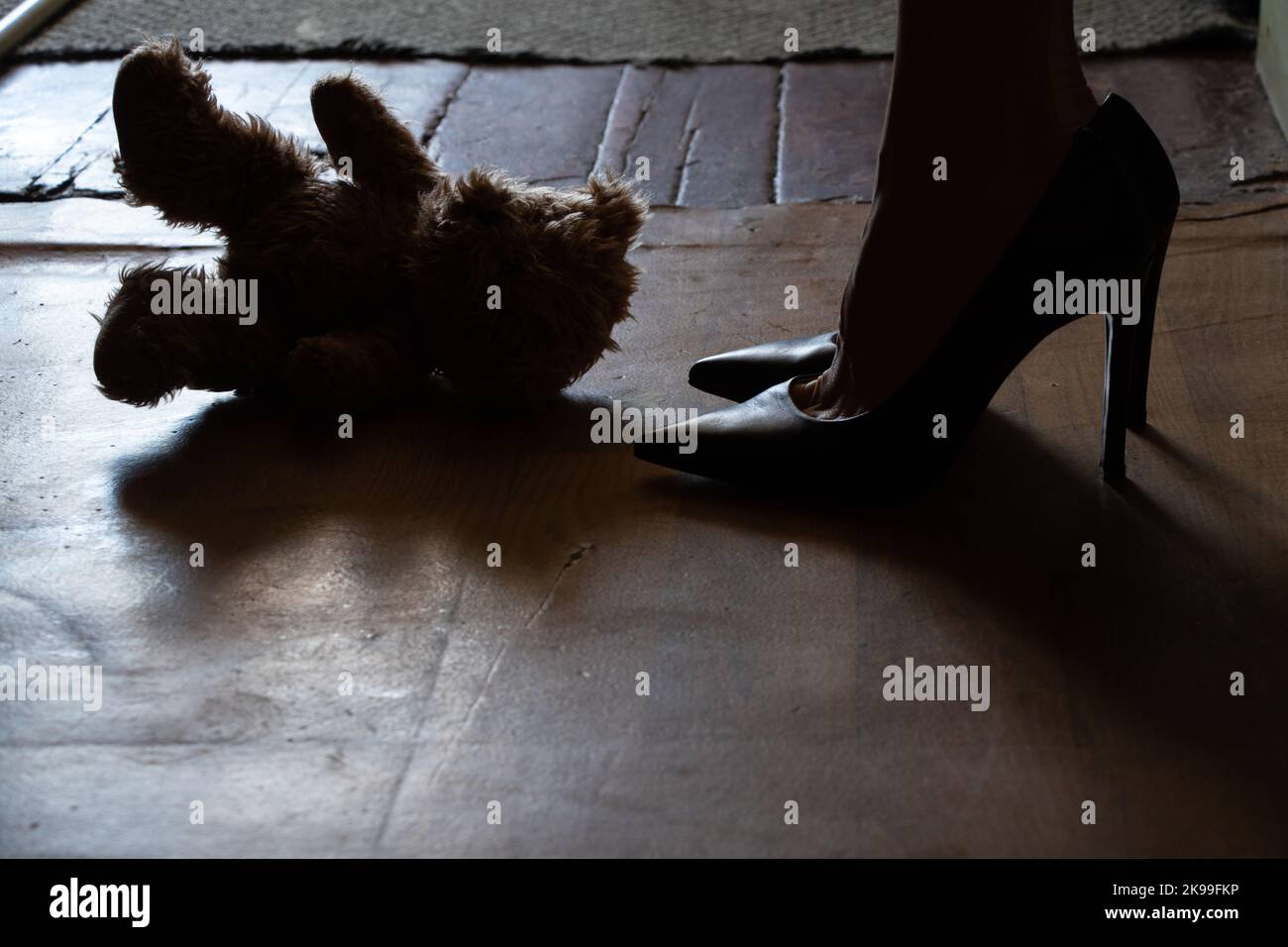 les pieds féminins à côté d'un ours en peluche sur le sol dans la nuit dans la chambre, un jouet de bébé jeté sur le sol Banque D'Images