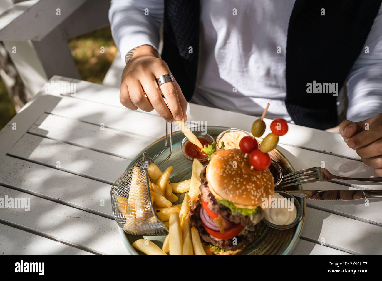 gros plan sur un hamburger dans une assiette et les mains d'un homme caucasien inconnu se préparent à manger sur la table dans la journée ensoleillée à l'extérieur au restaurant Banque D'Images